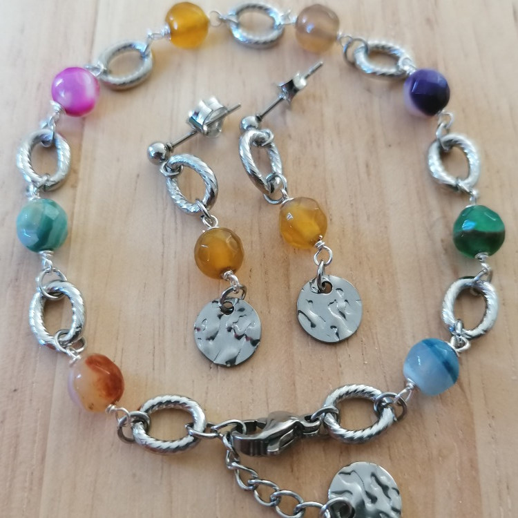 Armbånd og øreringe, Et detaljerigt sølvfarvet sæt med perler i grønne, blå og varme nuancer samt runde vedhæng med et råt, håndlavet præg.